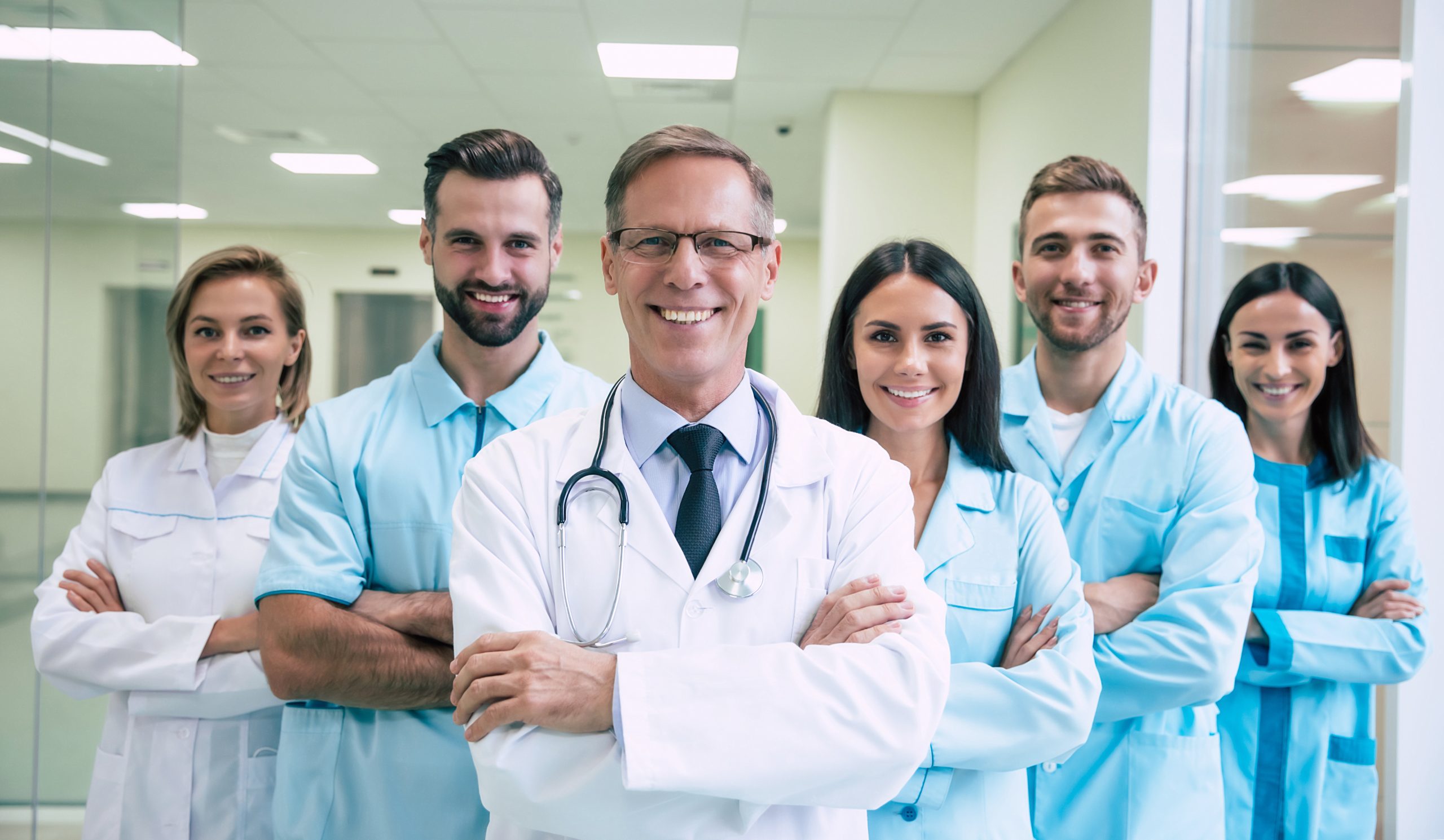 Happy team of successful and confident modern medical doctors are posing and looking on the camera at the hospital corridor